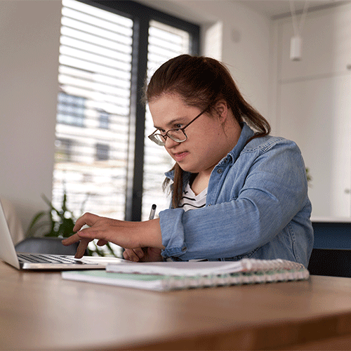 Young woman with disability using a laptop at home, representing inclusive disability and continence support services.